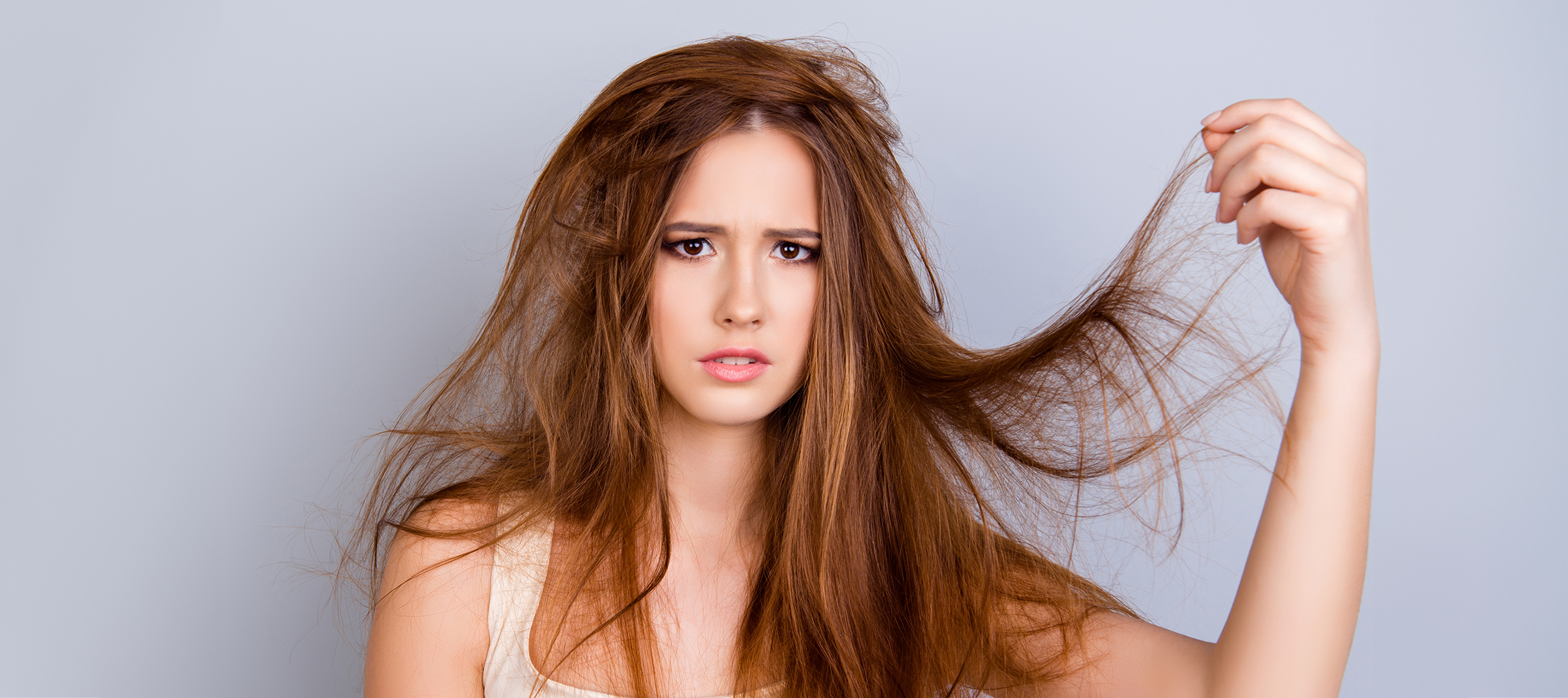 Close up portrait of frustrated young girl with messed hair on pure background, wearing white casual singlet, holding her hair